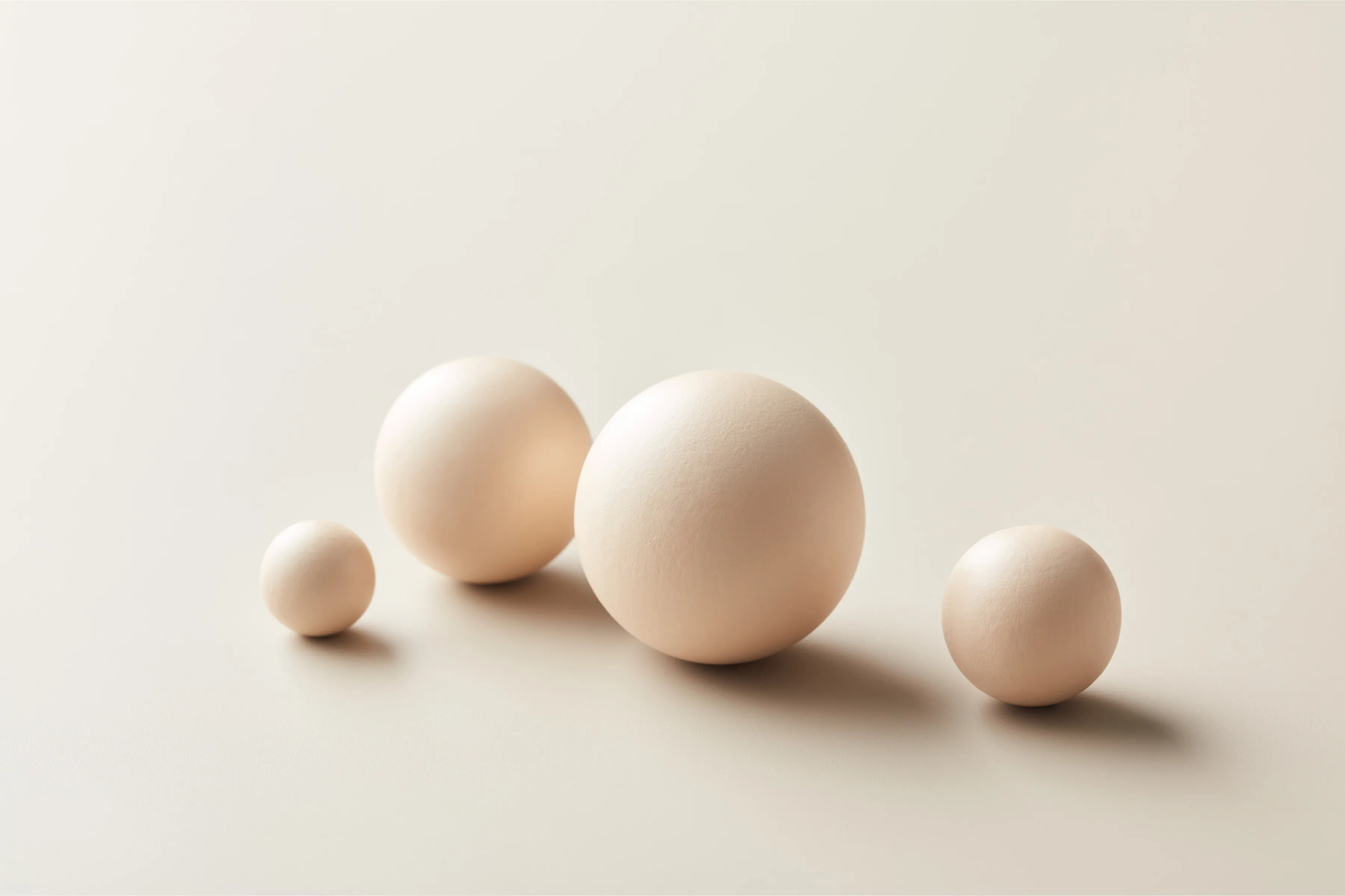 Four spheres of varying sizes aligned diagonally on a beige background with soft shadows.