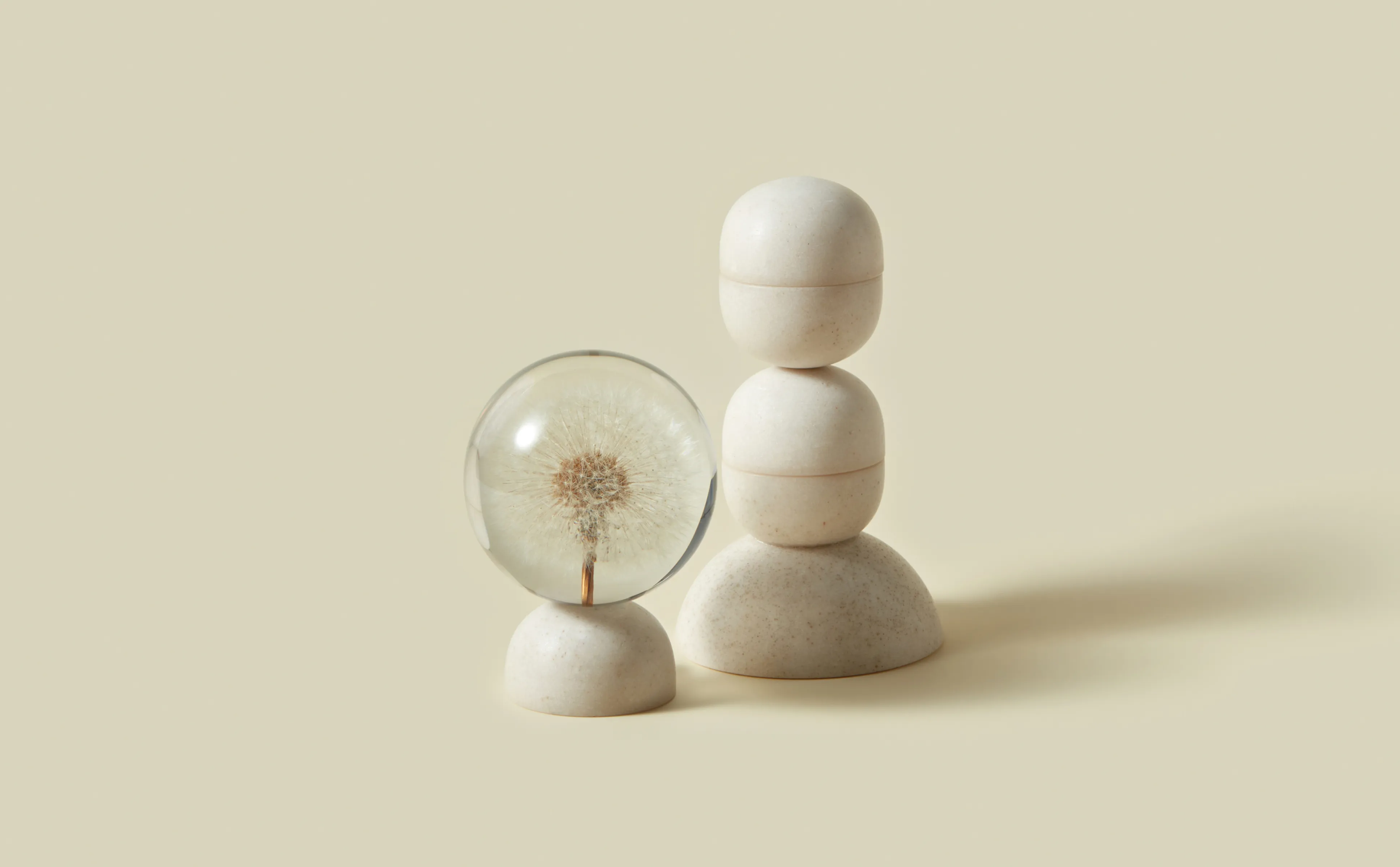 Three stacked zen stones with a magnifying glass focusing on a dandelion against a neutral background.